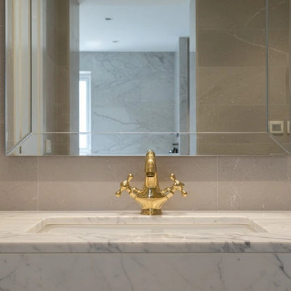 Bathroom sink with gold faucet and mirror on tiled wall